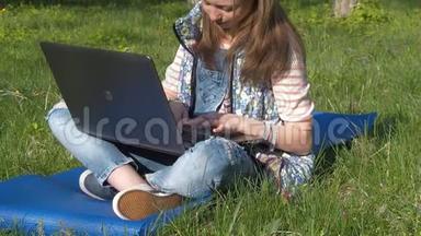 一个女孩坐在公园里拿着笔记本电脑。 一个十几岁的女孩坐在地毯上呼吸新鲜空气。 阳光明媚的一天，一个带着笔记本电脑的女孩